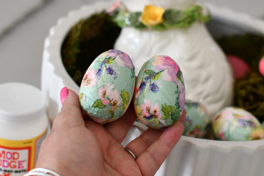 hand holding two decoupage eggs next to ceramic bunny