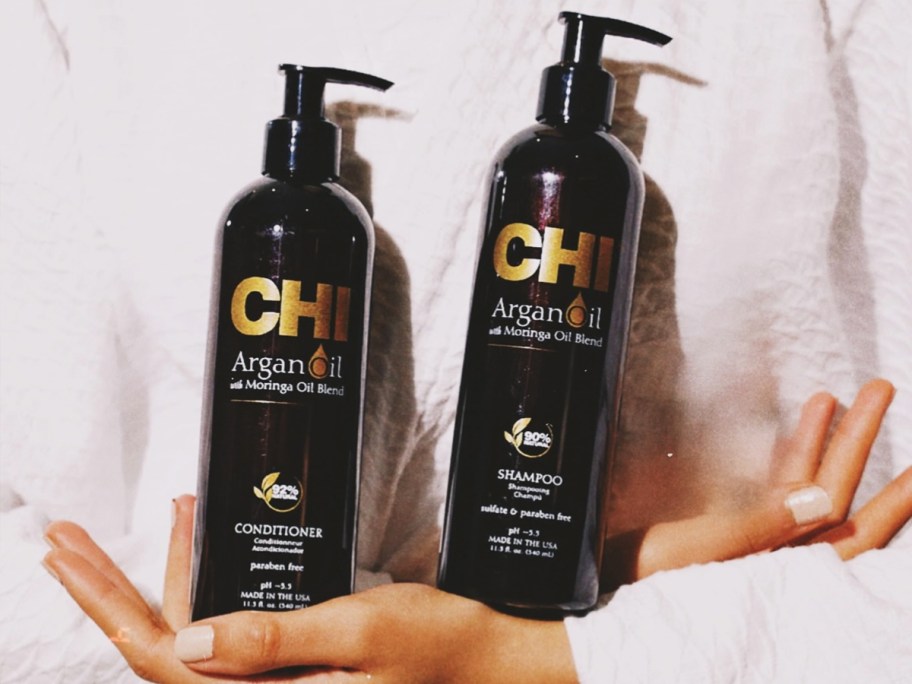 woman in white robe holding brown bottles of CHI Argan Oil Shampoo & Conditioner
