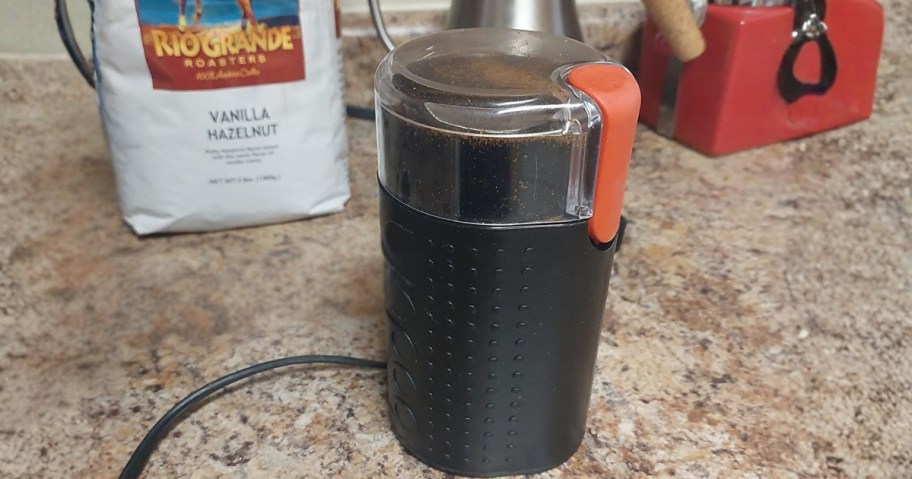 a small coffee grinder on a counter next to a bag of coffee and a coffee pot