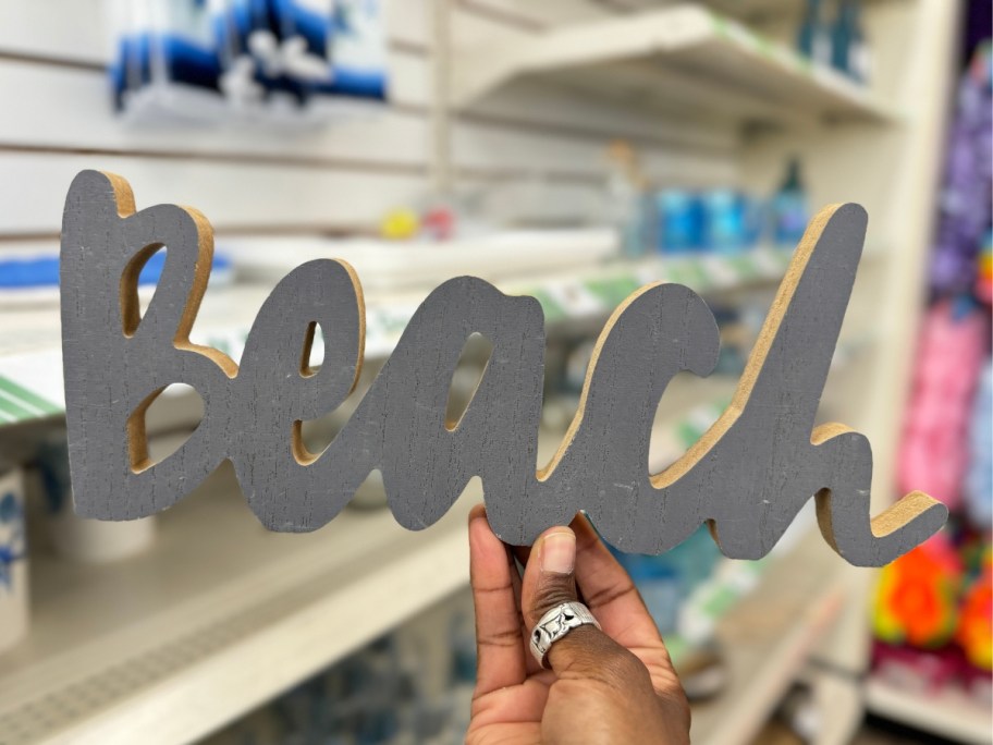 hand holding a gray wood sign with the word "Beach"