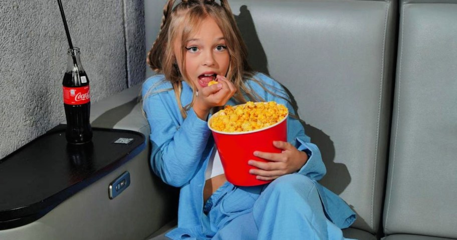 Child eating a big bucket of popcorn while watching a movie in a theater