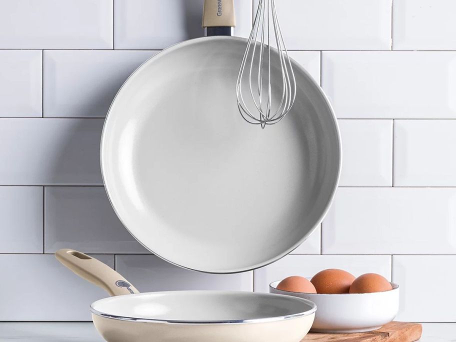 two greenpan frying pans displayed in the kitchen in front of another frying pan next to eggs