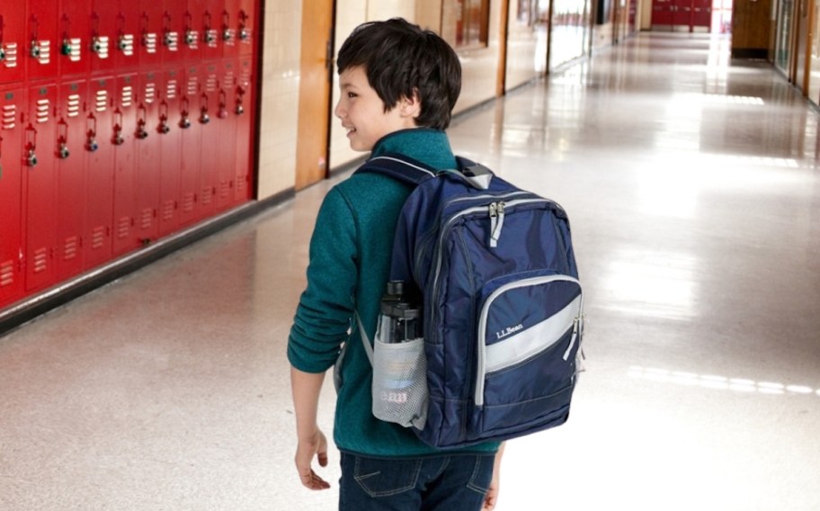 kid wearing navy ll bean bookbag in hallway with red lockers