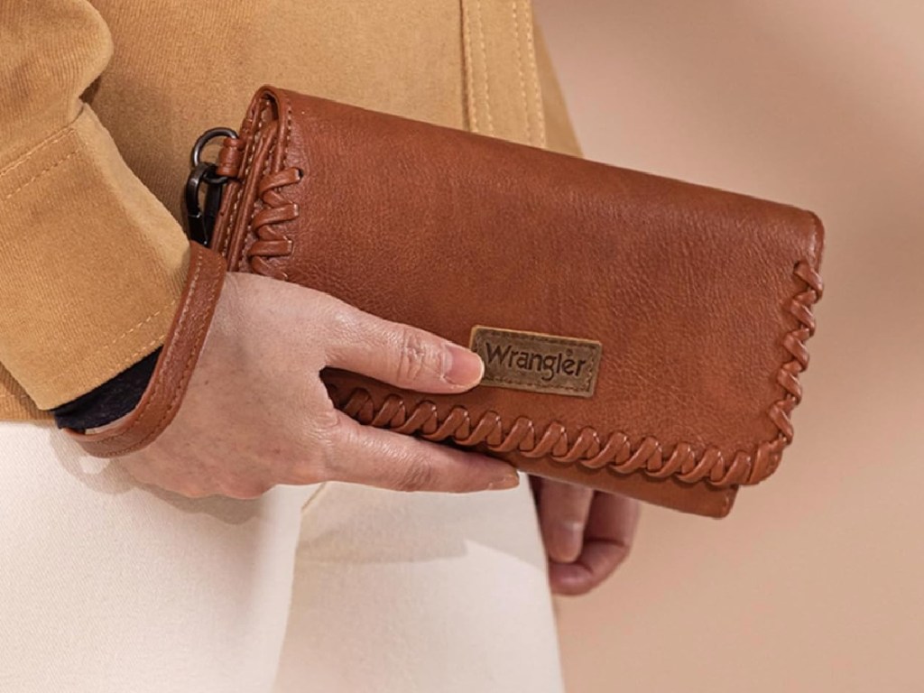 Woman carrying brown leather wrangler wristlet in her hand