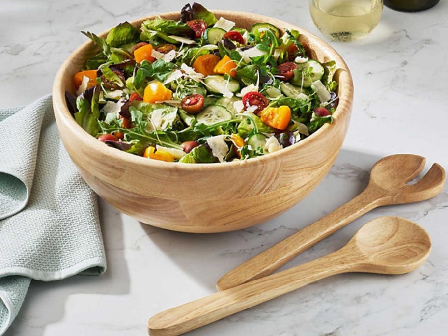 a wood salad bowl and serving spoons on a table
