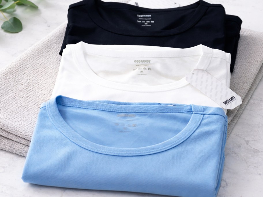 folded blue, white, and black t-shirts on a towel