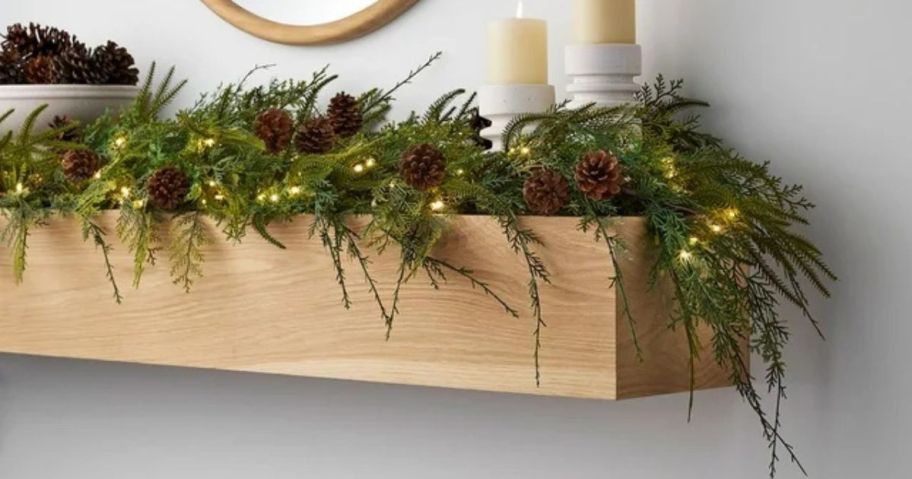 A mantle with greenery, pinecones, and a candle on it