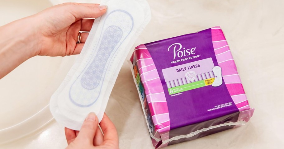 woman holding poise pad with bag laying next to her