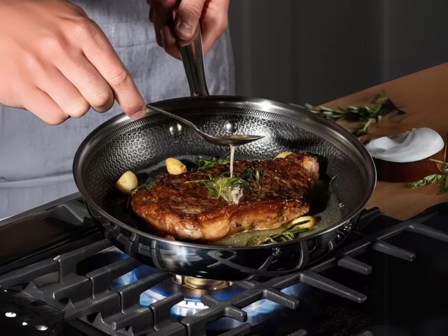 person holding T-Fal Hybrid Mesh Stainless Steel 10.5" Frypan on stove using a spoon to season meat inside of it