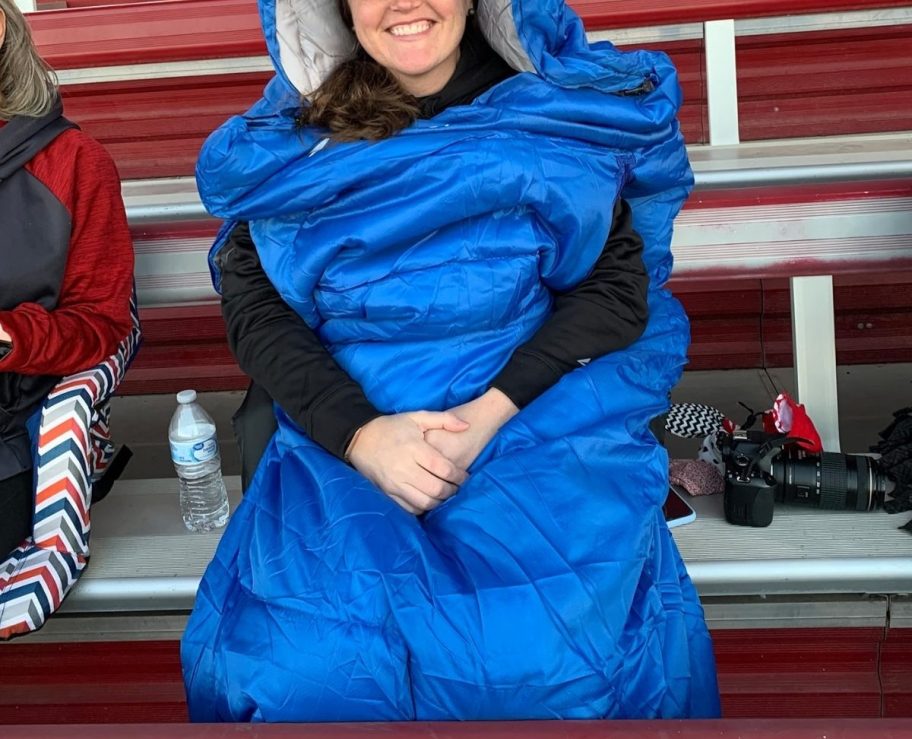 a woman in a blue wearable sleeping bag sitting on a bleecher