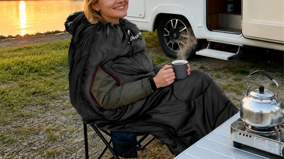 a woman in a wearable sleeping bag having a cup of coffee next to an RV