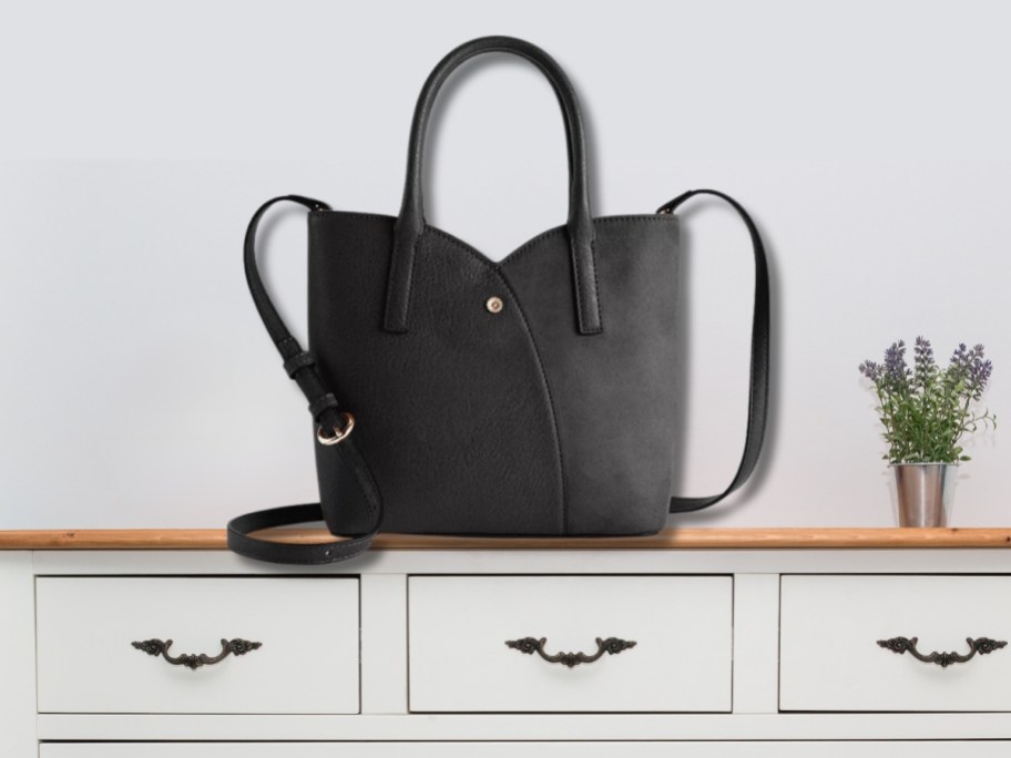 a large black tulip shaped handbag with shoulder strap on a console table