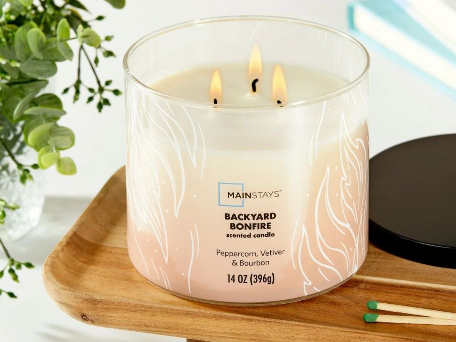 A lit Mainstays 3-Wick Candle in Backyard Bonfire scent