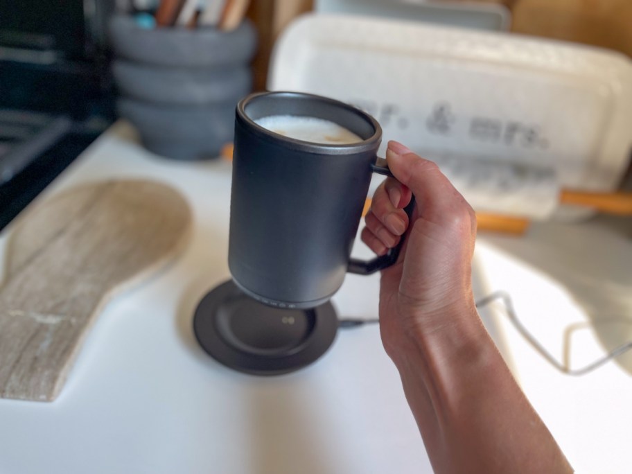Person holding up black coffee mug above warmer pad