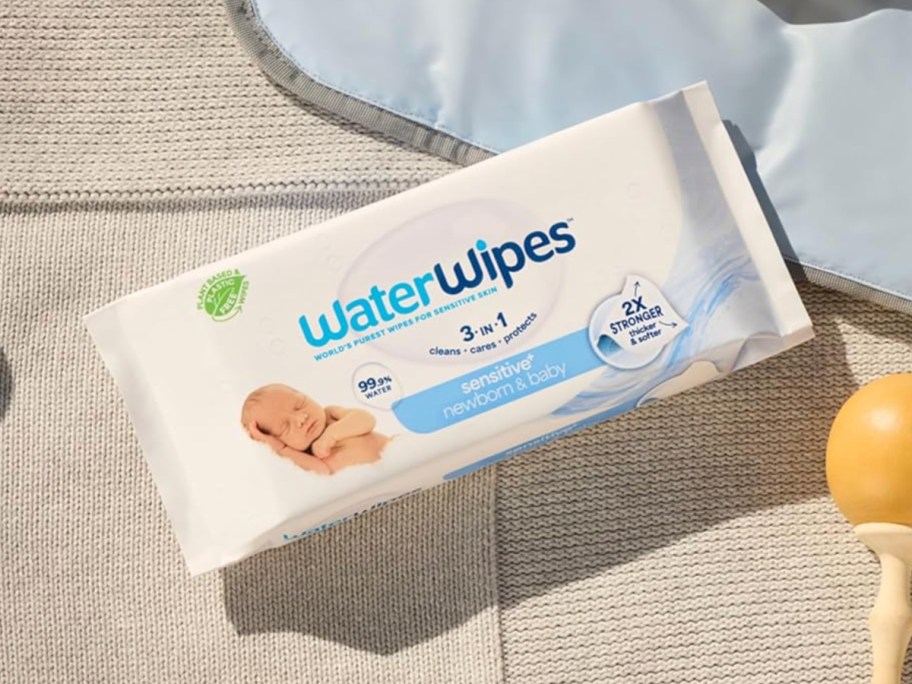 Package of water wipes next to baby blanket and rattle