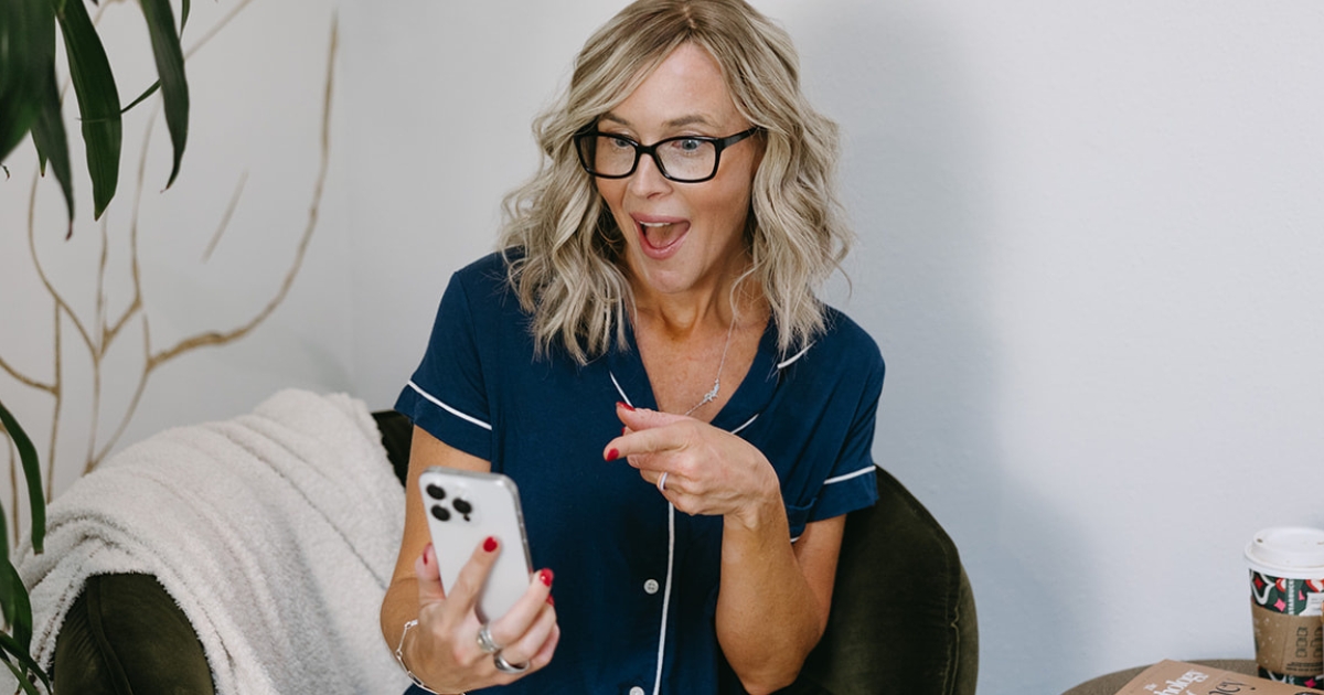 http://Woman%20holding%20up%20cell%20phone%20with%20one%20hand%20and%20pointing%20at%20the%20screen%20with%20her%20other%20hand