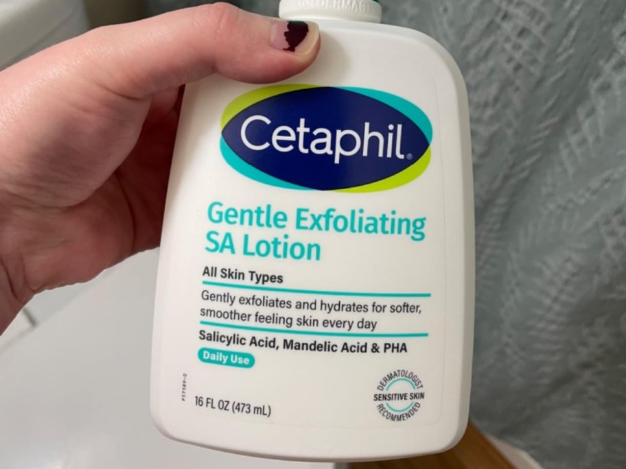 A hand holding up a bottle of Cetaphil lotion.