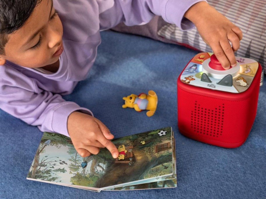 child playing with a red Tonie Box audio player with a Winnie the Pooh Tonie figure and book
