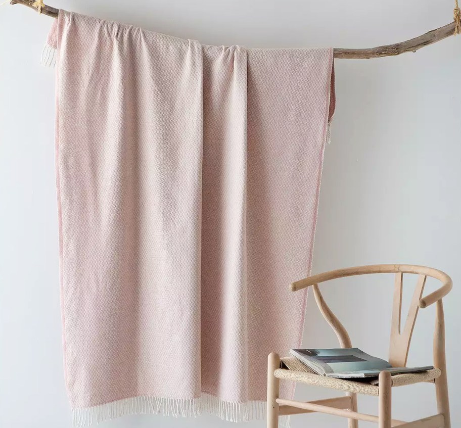 pink throw hanging from a branch near a chair