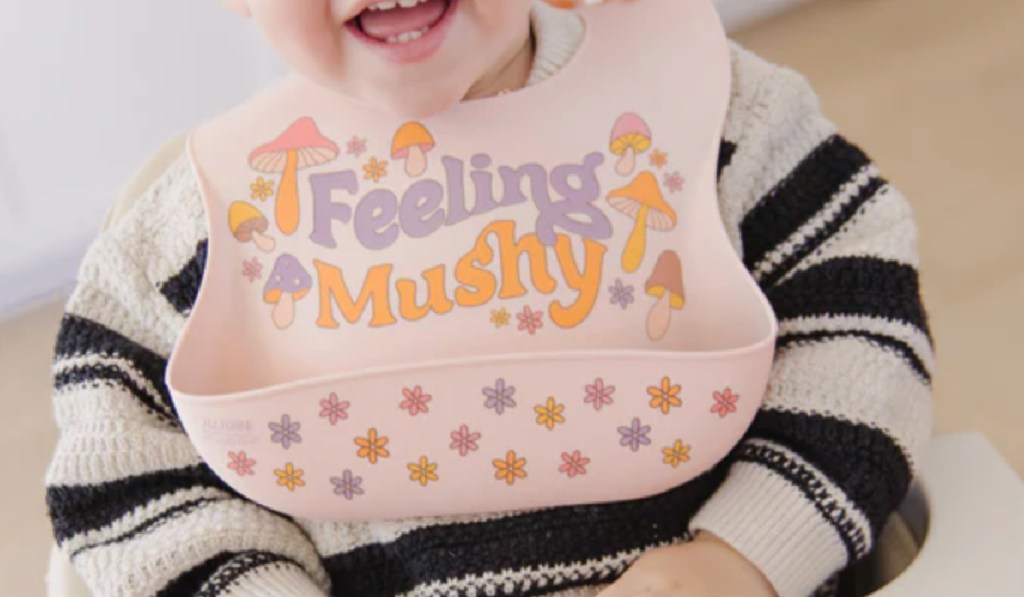 baby wearing pink feeling mushy bib while eating