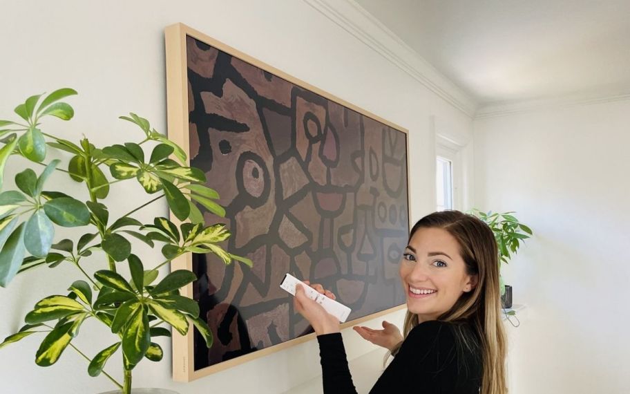 a woman with remote in front of a samsung frame tv