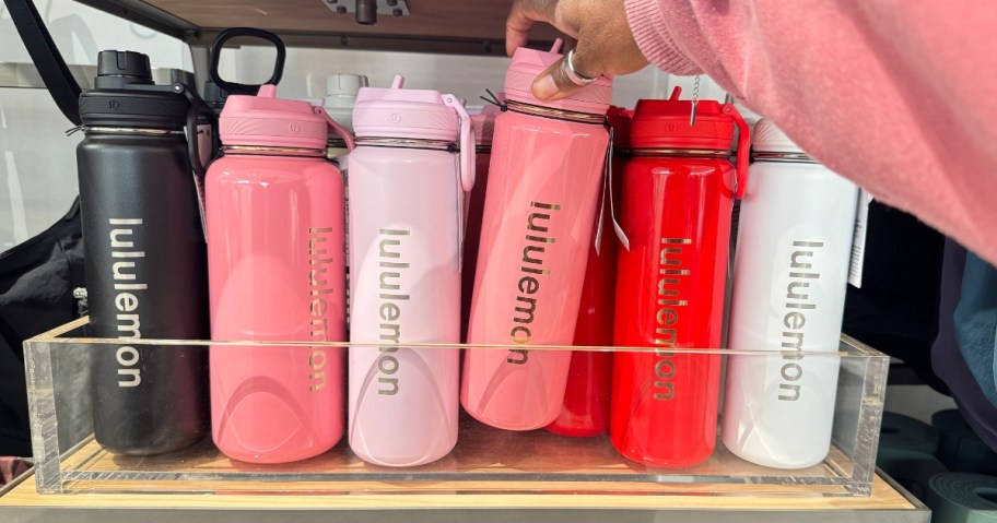 hand reaching for a lululemon water bottle on a shelf with more