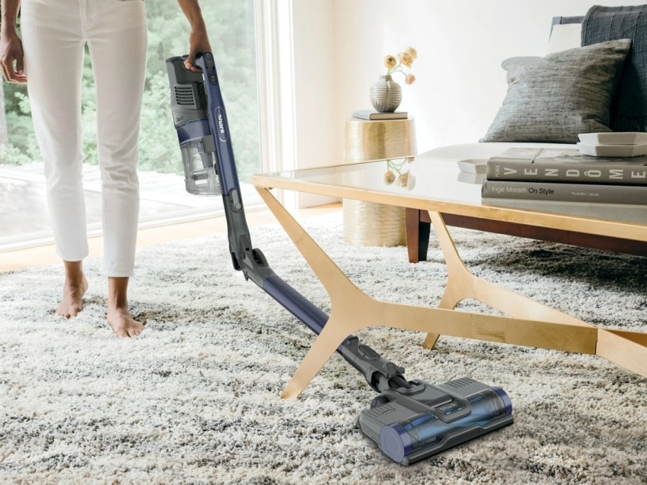 woman using shark pet pro cordless vacuum to vacuum area rug in living room