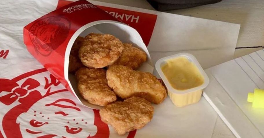 Wendy's chicken nuggets coming out of the container next to a pack of honey mustard sauce on a Wendy's paper wrapper