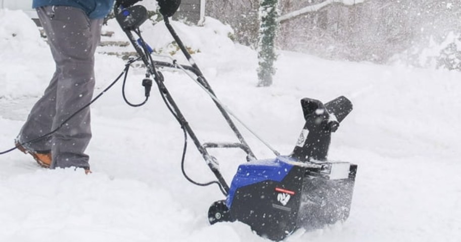 man using an electric snow blower to clear a driveway
