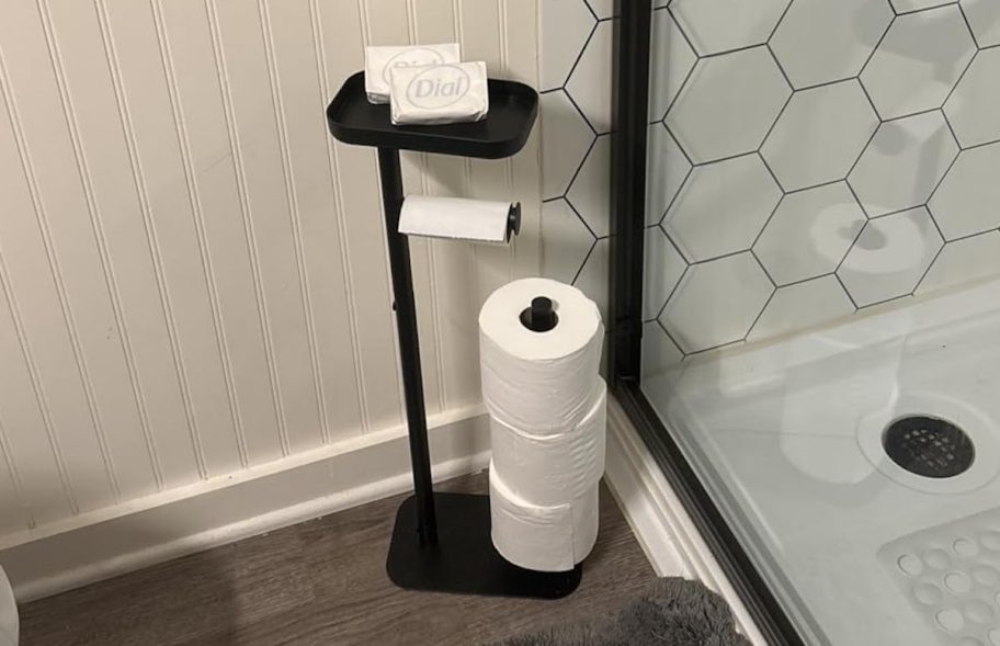 toilet paper holder stand on bathroom floor next to shower with soap on top