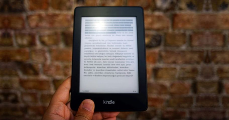 Hand holding up a kindle in front of a Brick wall