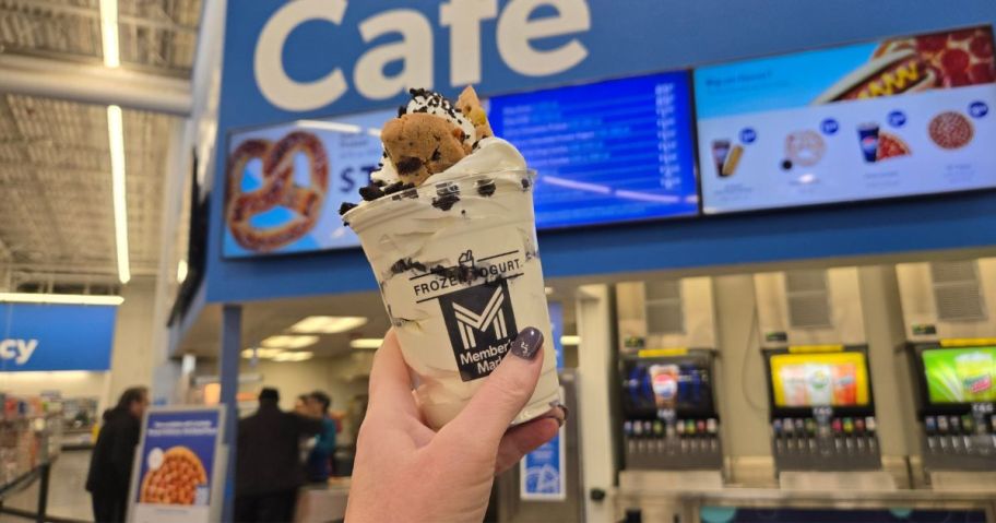 A person holding an ice cream sundae up in front of a cafe