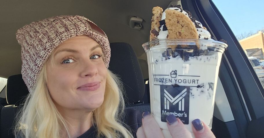 A blonde woman holding an ice cream sundae up in a car