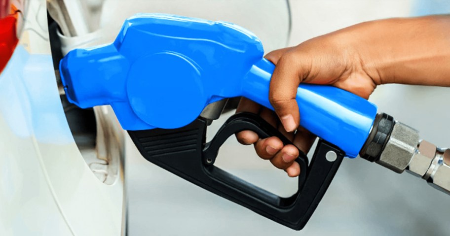 person holding a blue gas pump nozzle in their gas tank