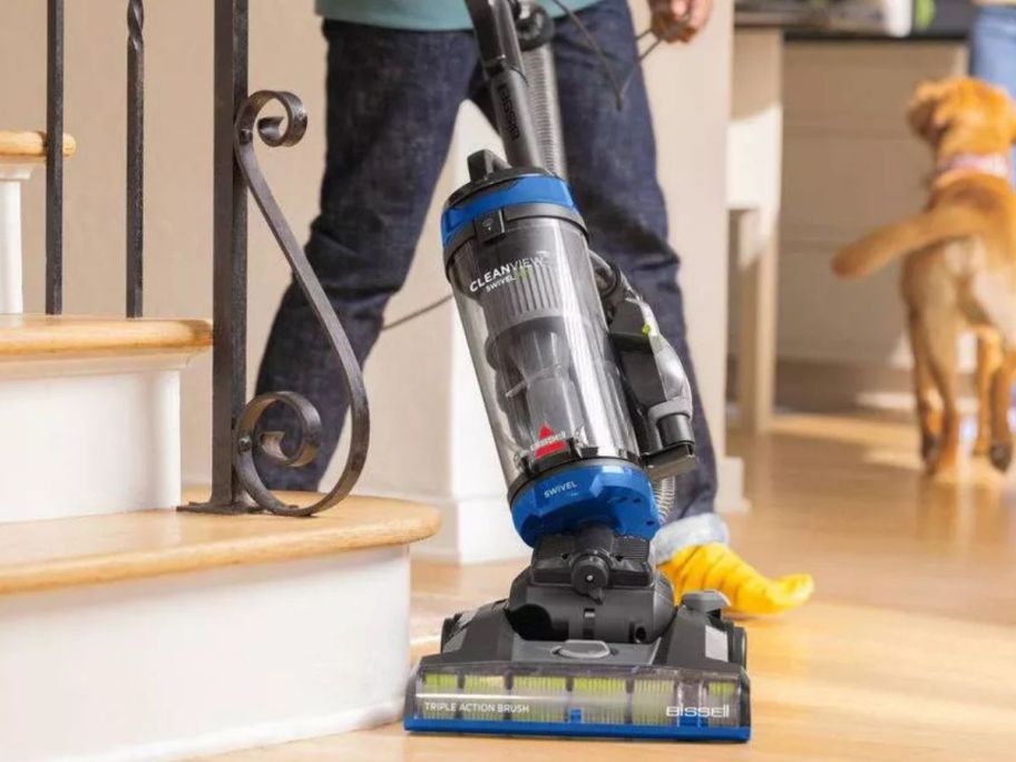 Man using a Bissell CleanView Swivel Pet Corded Vacuum with a golden retriever in the background