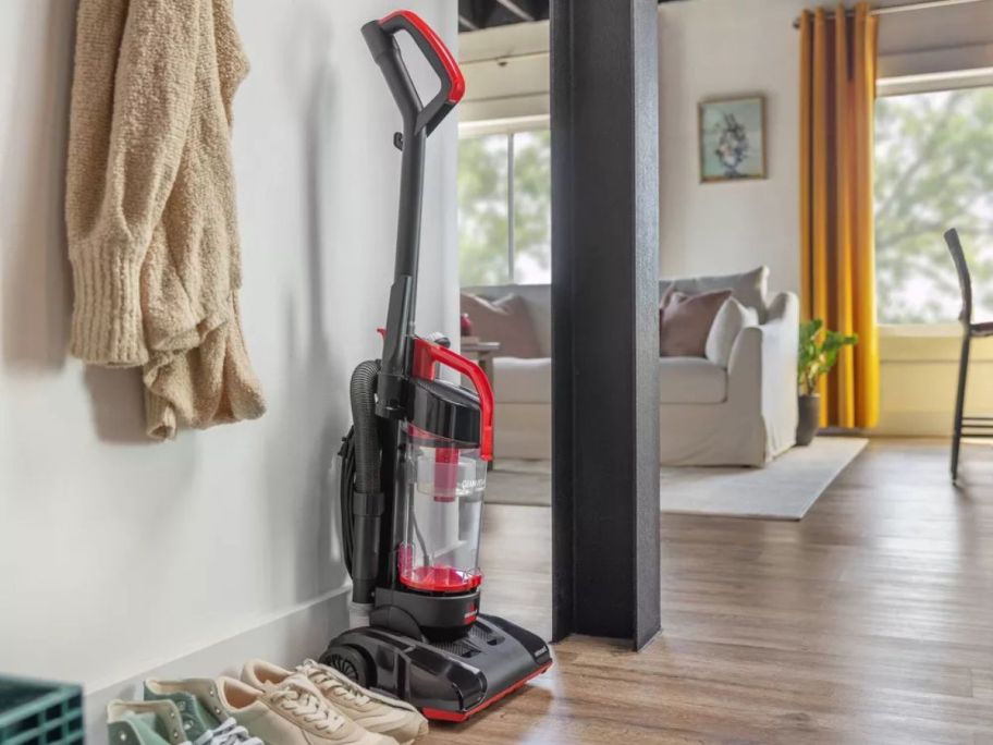 A Bissell CleanView Compact Upright Corded Vacuum up against a wall next to shoes and a coat rack