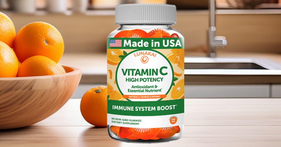 bottle of vitami c gummies on a kitchen counter next to a bowl of oranges