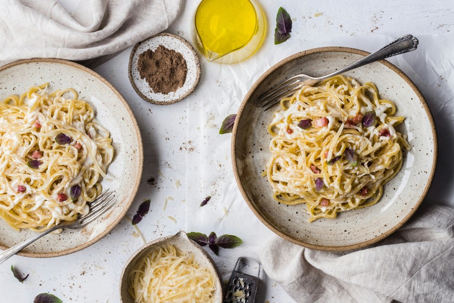 two plates with pasta on table with olive oil and spices