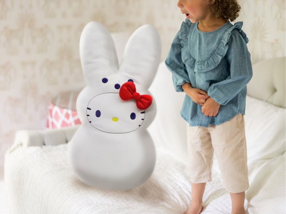 a little girl standing next to a jumbo size Peeps Hello Kitty plush