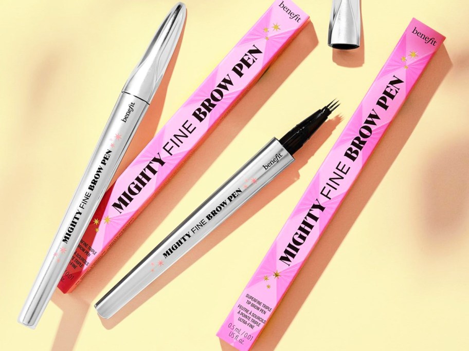 two Benefit Cosmetics Mighty Fine Waterproof Brow Pens and their boxes on a yellow background