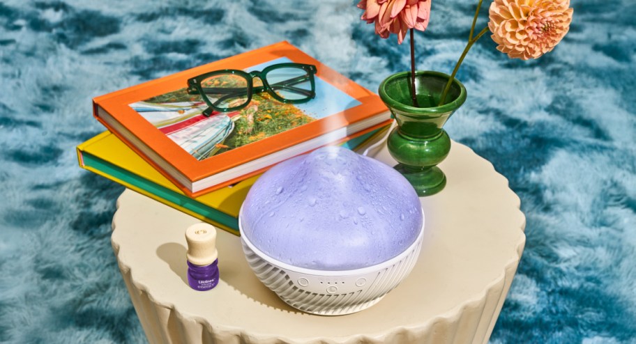 Diffuser displayd on top of the table with flowers and a notebook 