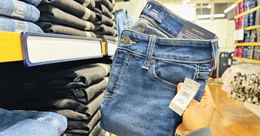 hand holding up a pair of folded gap jeans in store