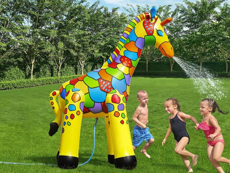 kids running around a huge giraffe water sprinkler