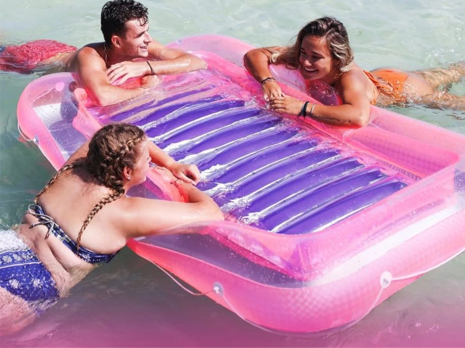 two teen girls and a teen boy with their arms resting on the sides of a Swimline Classic Edition Inflatable Suntan Tub Pool Lounger while in a pool