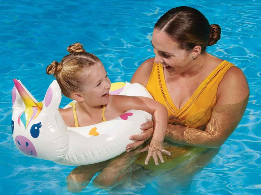 mom holding a little girl in unicorn pool float in a pool