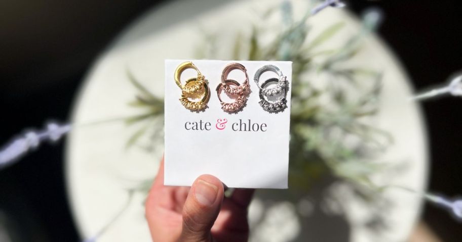 person holding cate & chloe box with gold, rose gold, and silver pairs of earrings on it