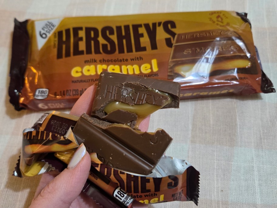 holding a broken caramel bar next to a Hershey's wrapper