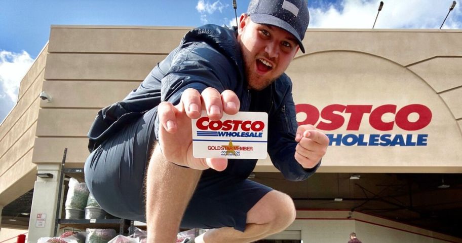 Man crouching in front of a Costco Warehouse while holding a Costco Card