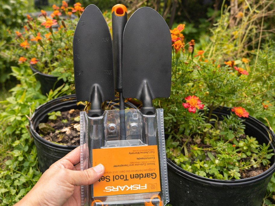 hand holding a set of garden tools in front of potted plants