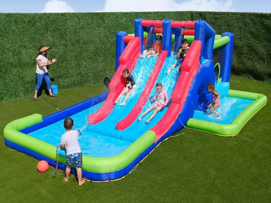 Large inflatable waterpark with two slides filled with water and several children playing